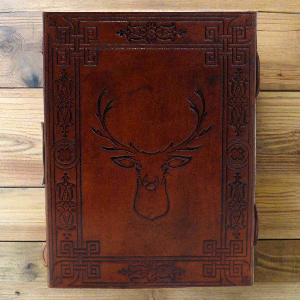 Antiqued leather journal with burnt edges and classic closure, open to eco-friendly pages, styled on a cosy wooden desk.