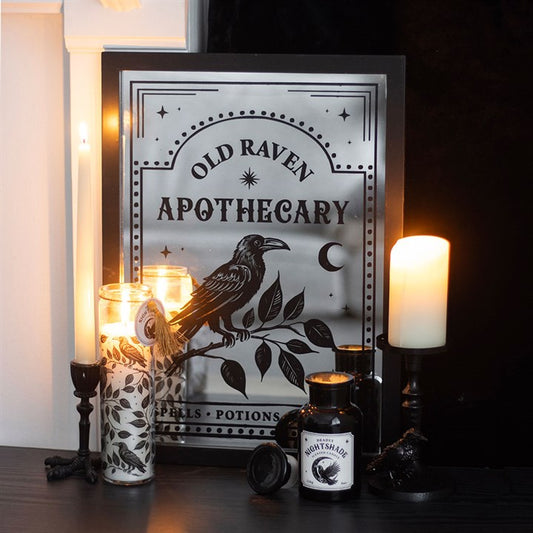 Decorative setup with 'Old Raven Apothecary' sign, candles, and bottles on a dark surface.