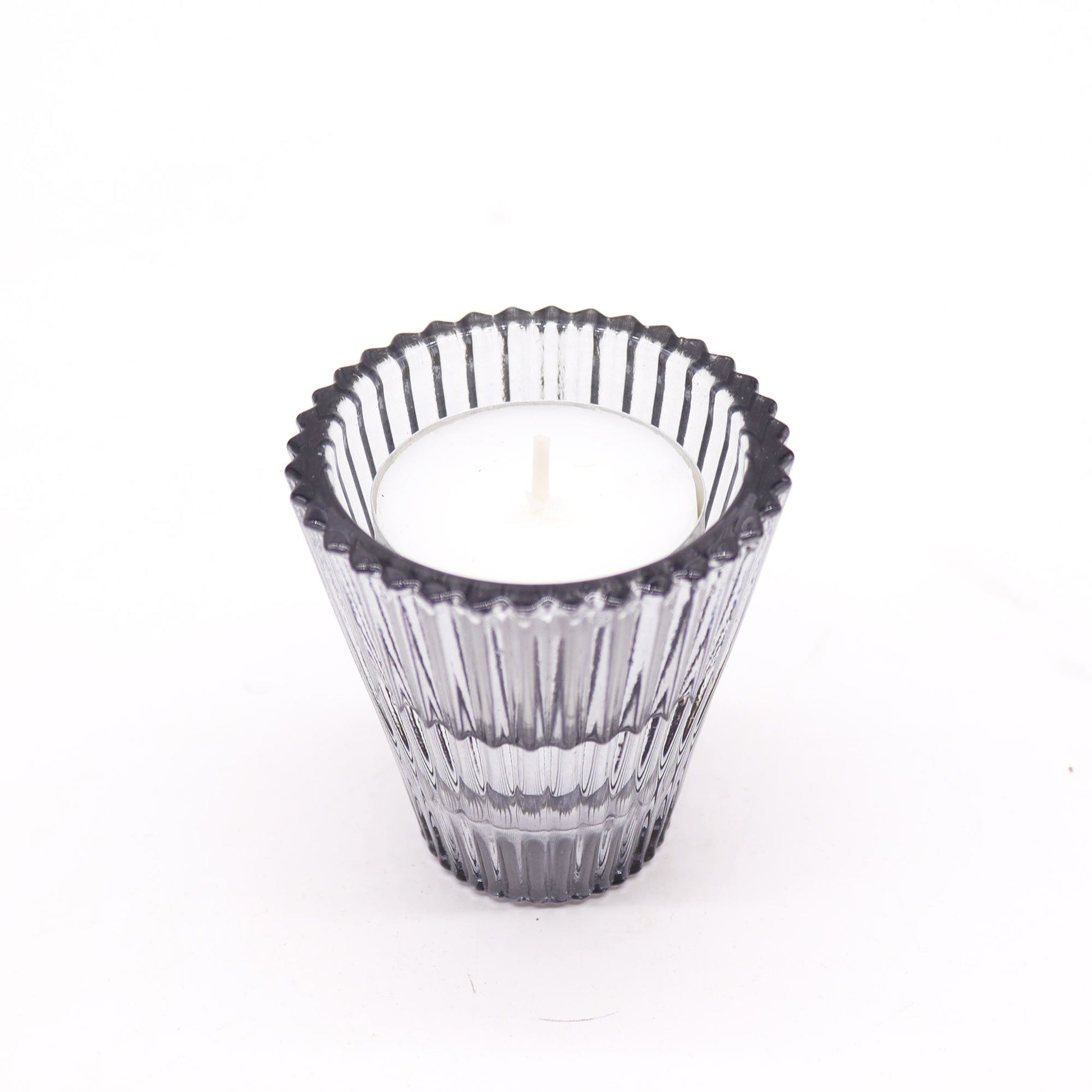Clear glass candle holder with a white candle on a white background