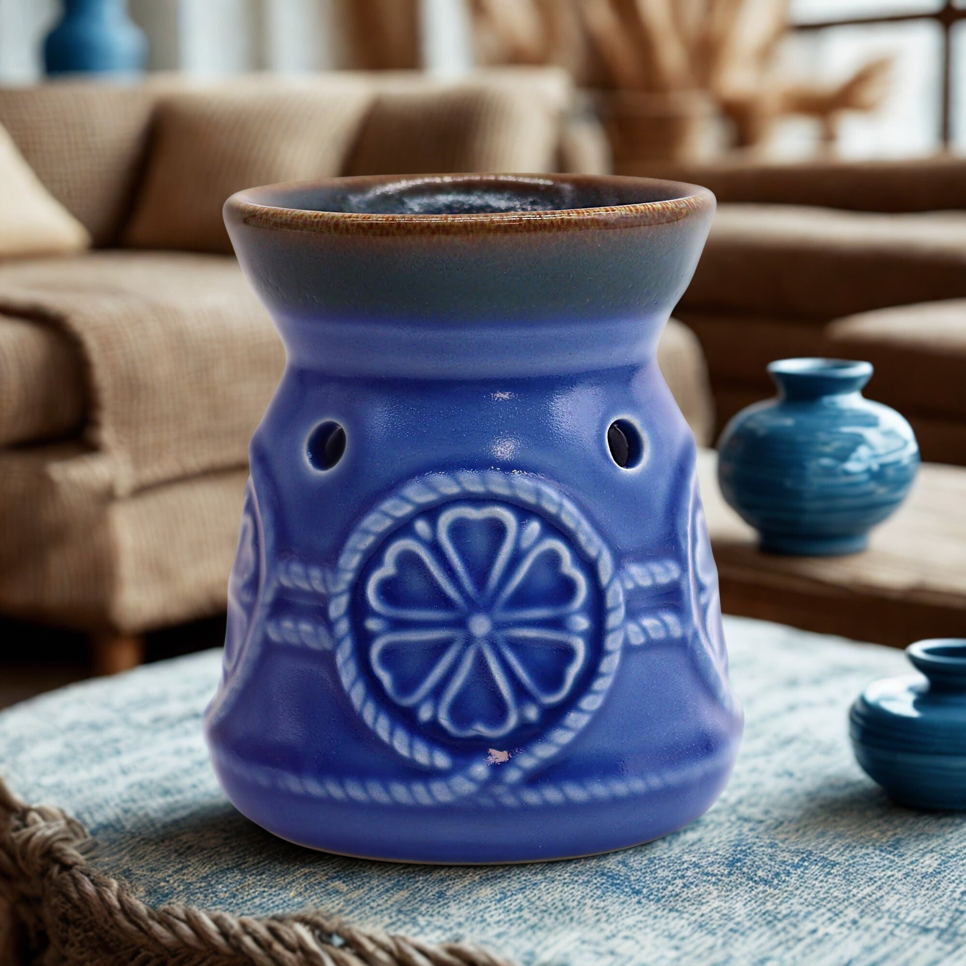 Blue ceramic oil burner on a woven tray, softly lit for a cosy lifestyle setting.
