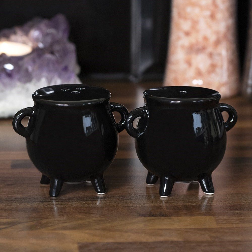 Two glossy black mini cauldron salt and pepper shakers on a wooden countertop.