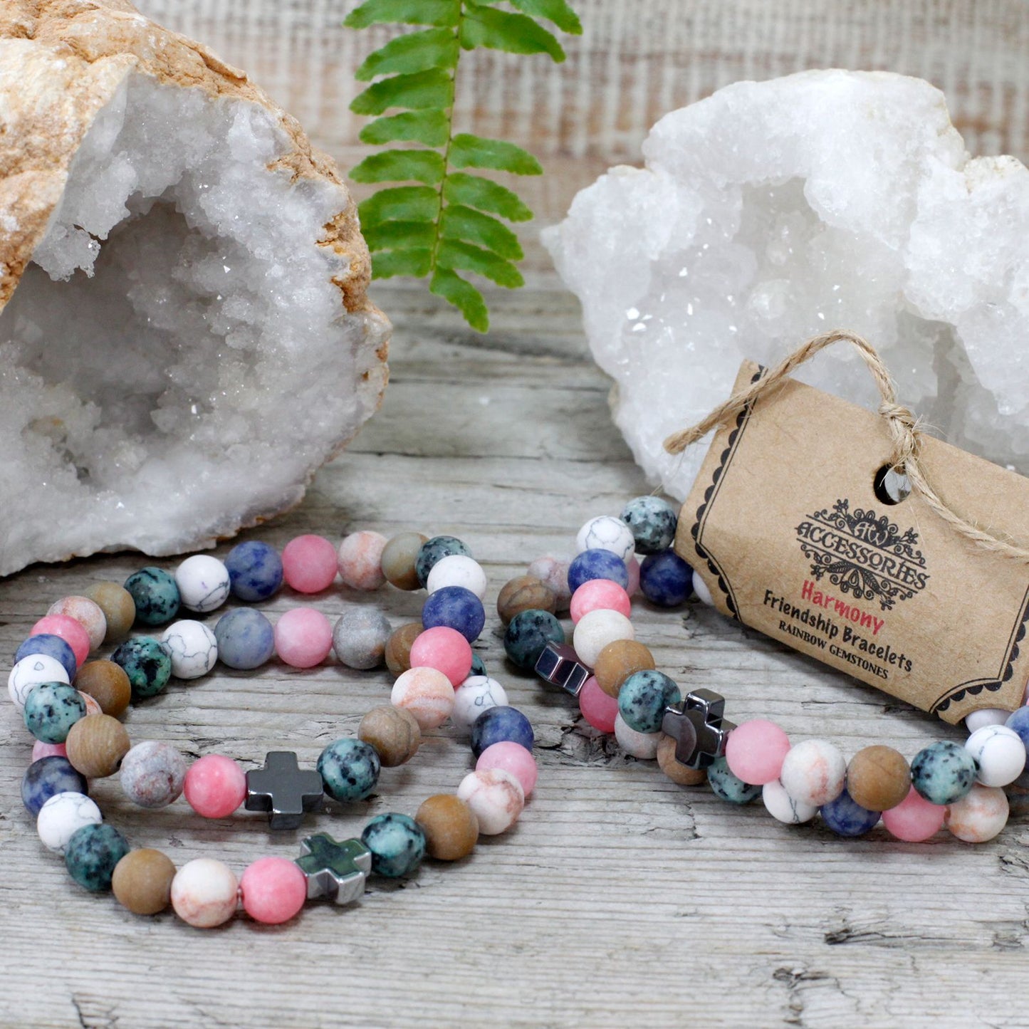 Two rainbow gemstone friendship bracelets on rustic wood with crystal geodes.
