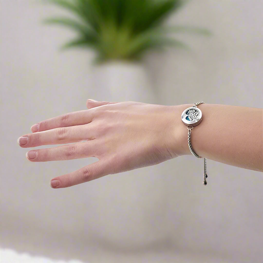 Stainless-steel Tree of Life diffuser bracelet with green felt pad inside a 20 mm locket displayed on a wrist.