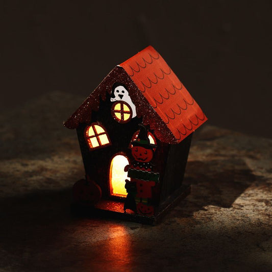 Small black Halloween house with an orange roof and glitter trim, warm LED glow in the door and windows, pumpkins, ghost, and “Trick or Treat” sign.