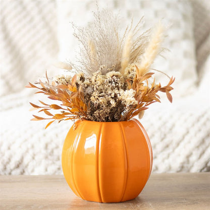 Orange pumpkin-shaped vase with dried flowers on a wooden surface