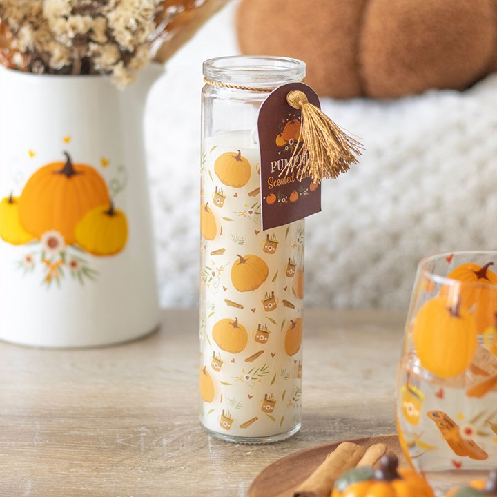Glass candle with pumpkin design and decorative tag on a wooden surface.