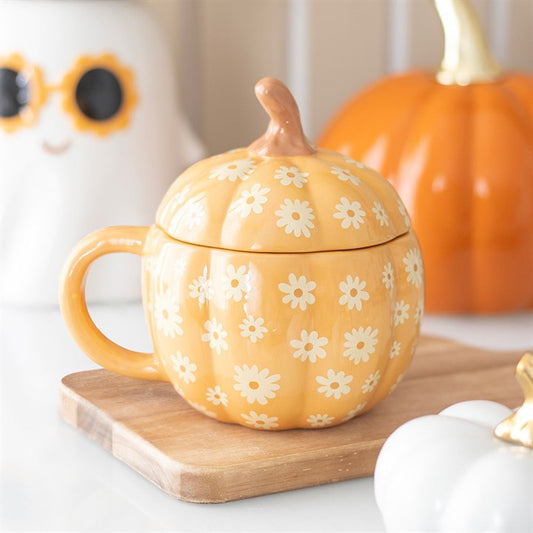 Orange pumpkin-shaped mug with floral design on a wooden board, with pumpkins in the background.