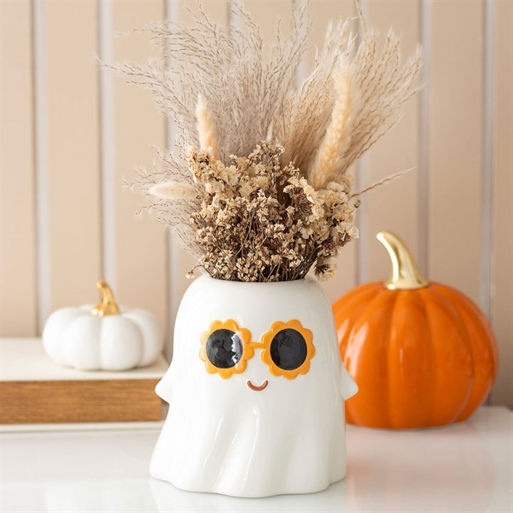 Decorative ghost vase with dried flowers, surrounded by pumpkins on a neutral background