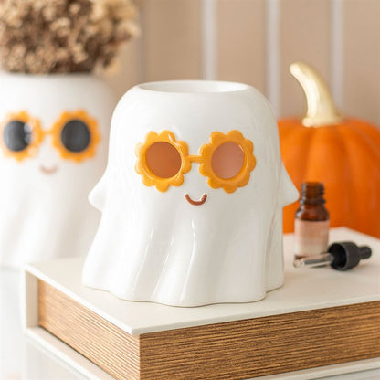 White ghost-shaped container with sunflower sunglasses on a shelf with a pumpkin and bottle in the background.