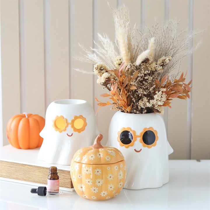 Decorative items including a ghost-shaped container, pumpkin-shaped container, and dried floral arrangement on a shelf.