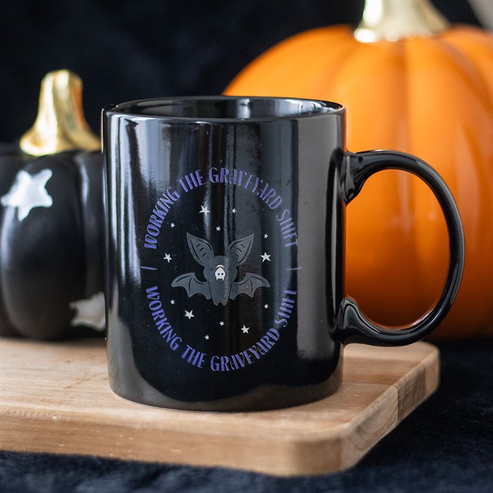 Black mug with bat design and text on a wooden board with pumpkins in the background