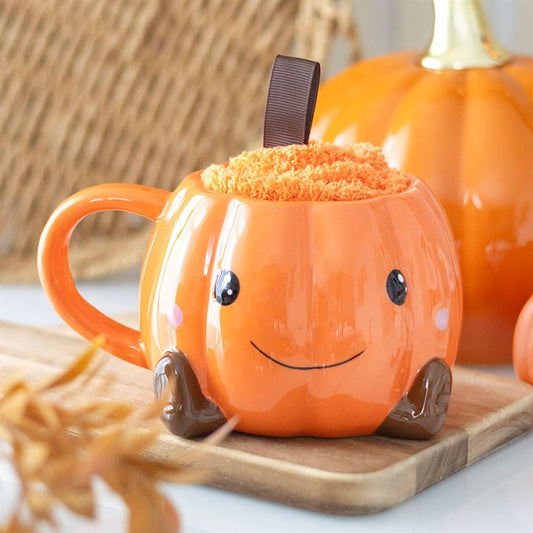 Pumpkin-shaped mug with a face on a wooden board with pumpkins in the background