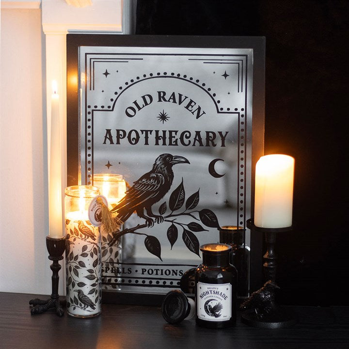 Decorative setup with 'Old Raven Apothecary' sign, candles, and bottles on a dark surface.