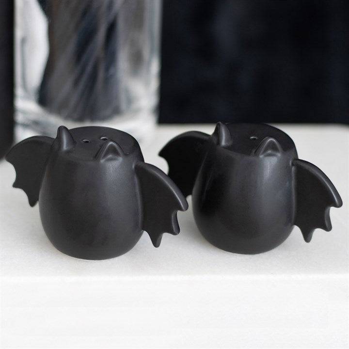 Two black bat-shaped salt and pepper shakers on a white surface with a blurred background.