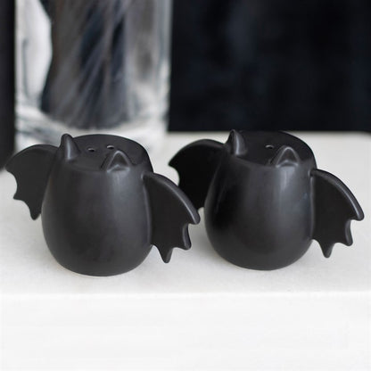 Two black bat-shaped salt and pepper shakers on a white surface with a blurred background.