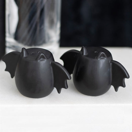 Two black bat-shaped salt and pepper shakers on a white surface with a blurred background.