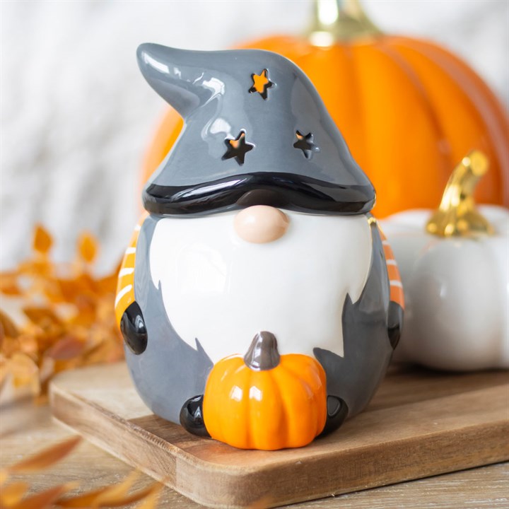 Halloween-themed gnome figurine with a witch hat and pumpkin on a wooden surface.