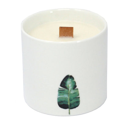 Candle in a white container with a green leaf design on a white background