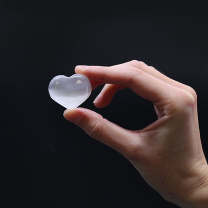 Hand holding a clear heart-shaped crystal against a black background