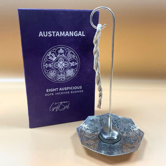 Silver incense burner with rope and purple packaging labeled 'Austamangal' on a beige background