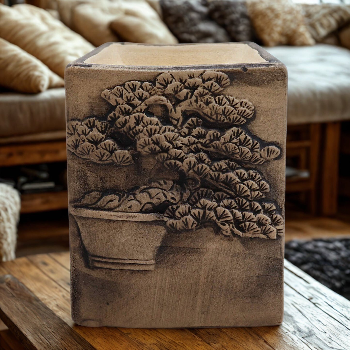 Hand-painted slate ceramic oil burner with carved bonsai design on a wooden table in a cosy living room.