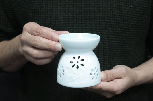 Close-up of a glossy white ceramic oil burner with petal-shaped cut-outs