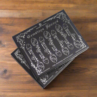 Black illustrated lid reading “Gemstone Spoons – For Modern Witchcraft” with silver botanical artwork.