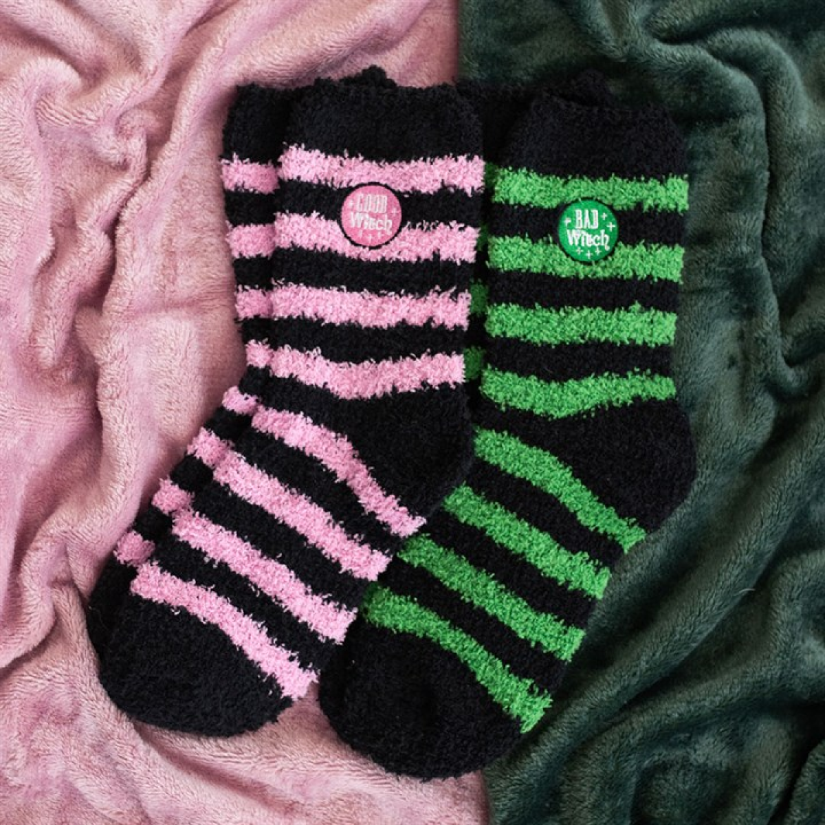 Two pairs of fluffy striped socks in black/pink and black/green with “Good Witch” and “Bad Witch” badges