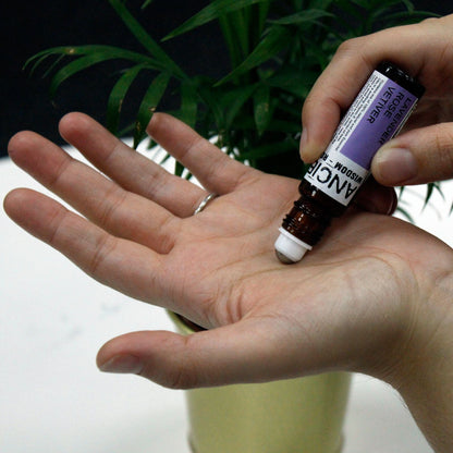Small amber glass roller bottle with black cap and stainless-steel ball, labelled ‘Just Chill! Lavender • Rose • Vetiver,’ shown being rolled onto the palm/wrist for pulse-point use