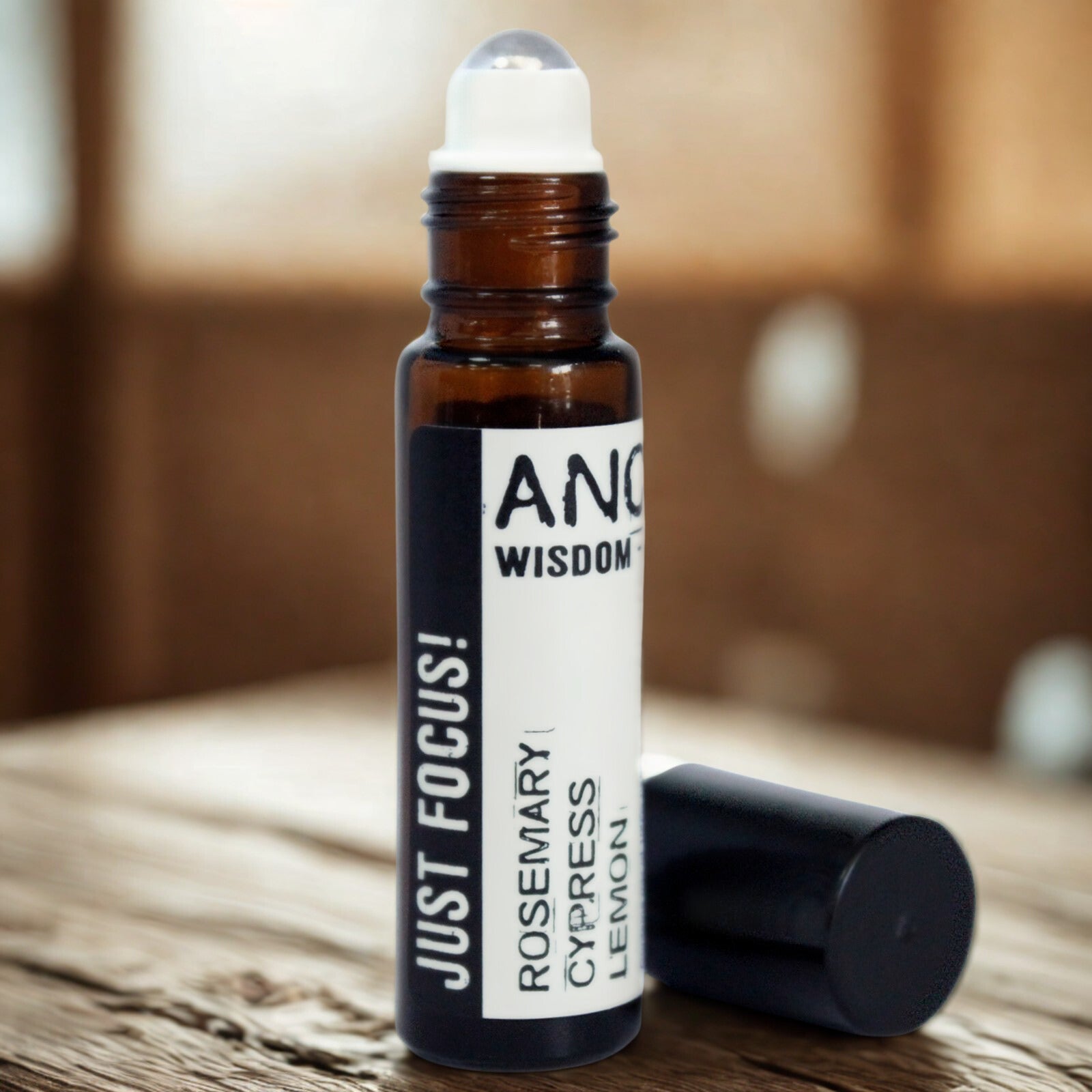 Small amber glass roller bottle with black cap and stainless-steel ball, labelled ‘Just Focus! Rosemary • Cypress • Lemon,’ shown open for pulse-point application.