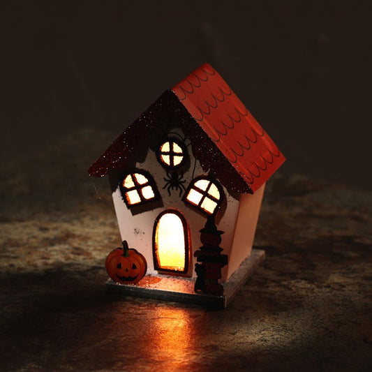 Lit pumpkin house LED decoration with orange roof and spider windows glowing on a dark surface.