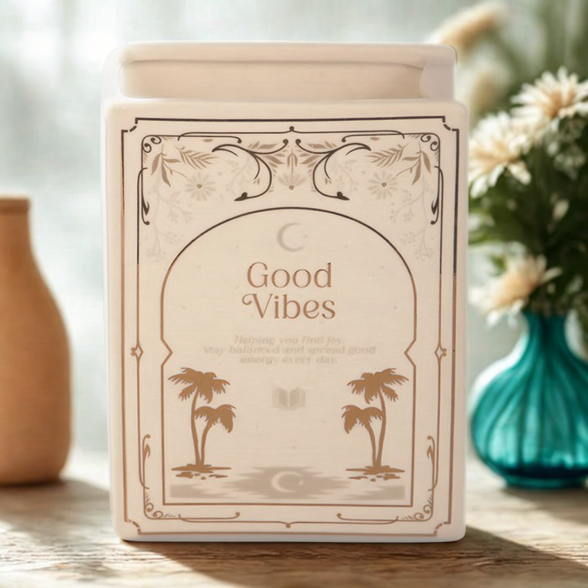 White ceramic book-shaped vase with gold ‘Good Vibes’ design, styled with flowers on a cosy tabletop