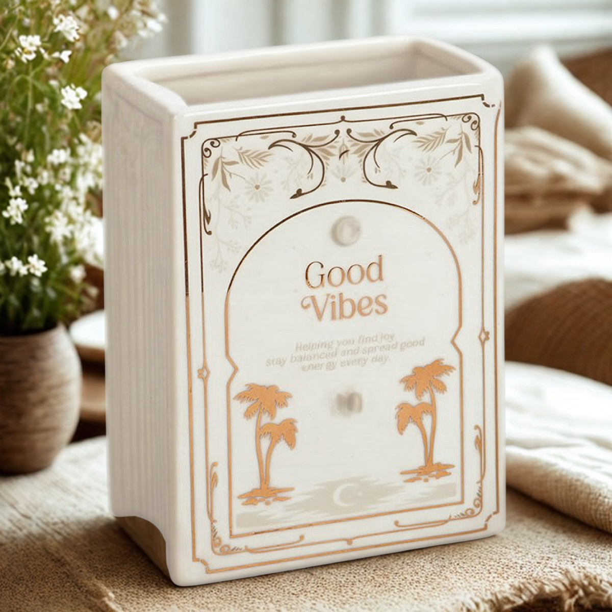 White ceramic book-shaped vase with gold ‘Good Vibes’ design, styled with flowers on a cosy tabletop